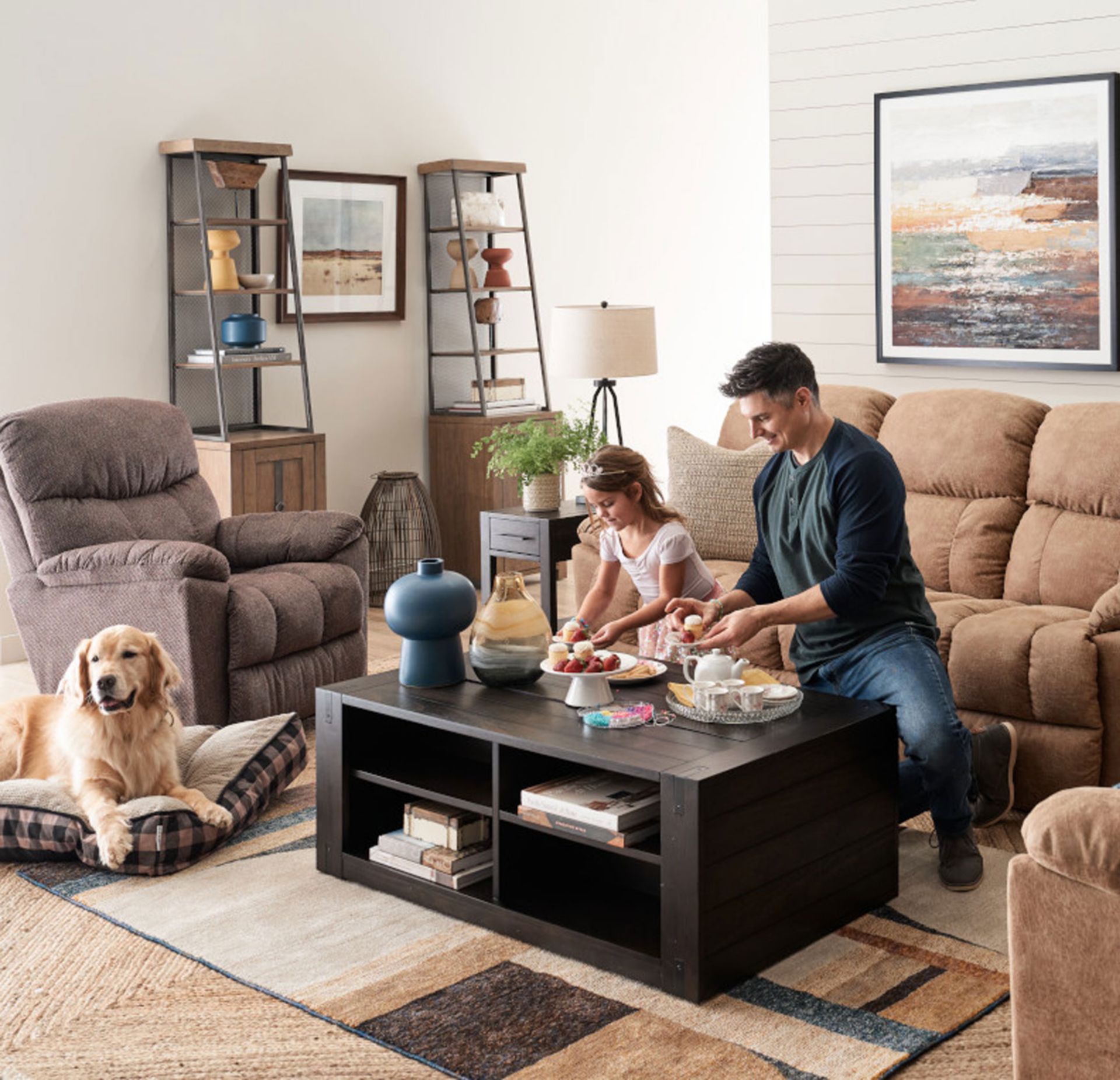 Man and his daughter having a tea part at the coffee table surrounded by morrison lazboy sofa set and golden retriever