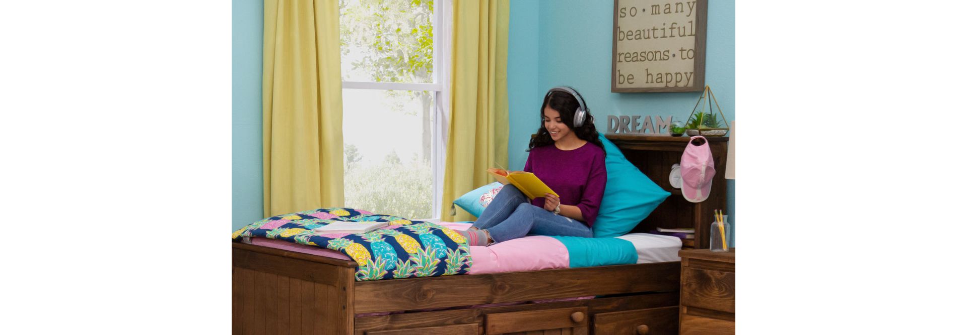 Student sitting on bookcase storage bed with headphones on and book