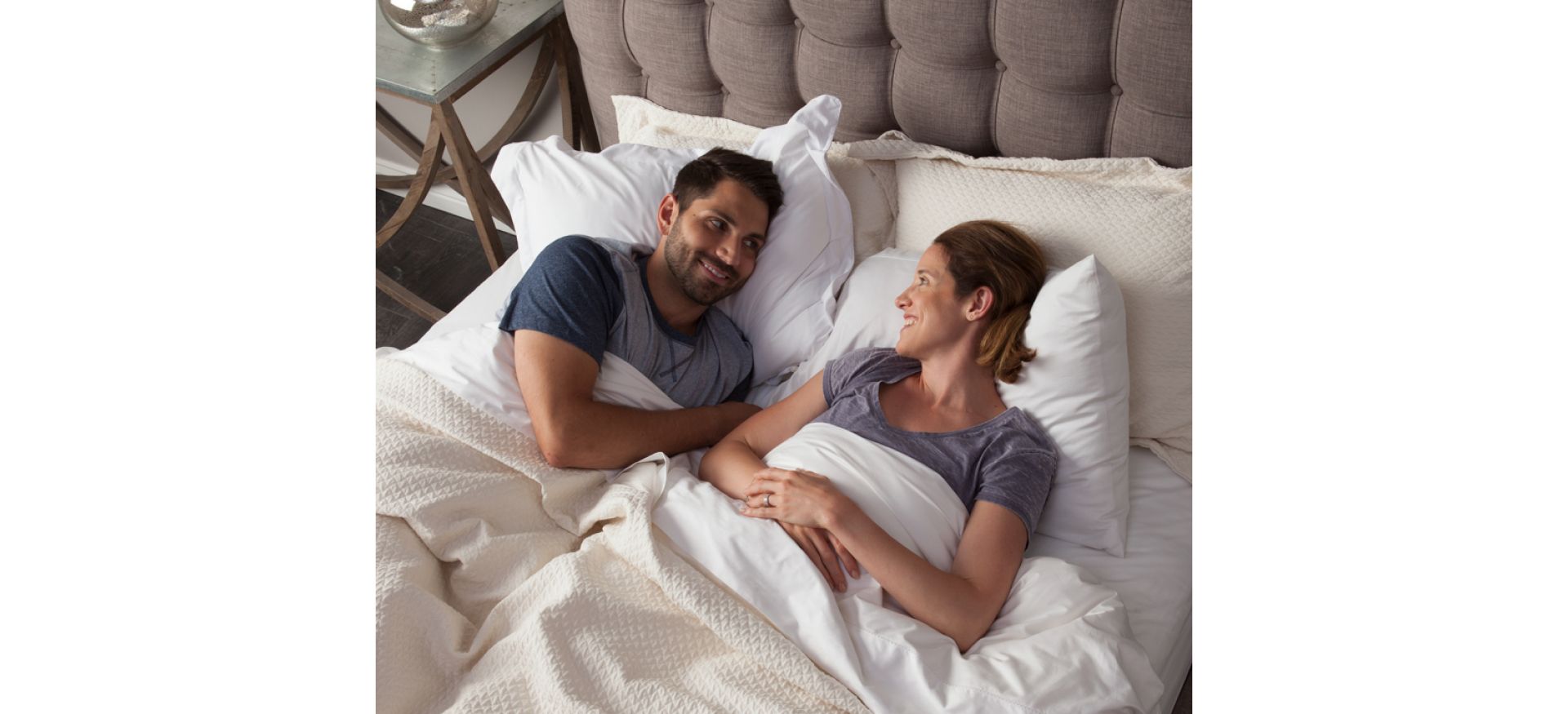 man and woman laying in bed together gazing into each other's eyes