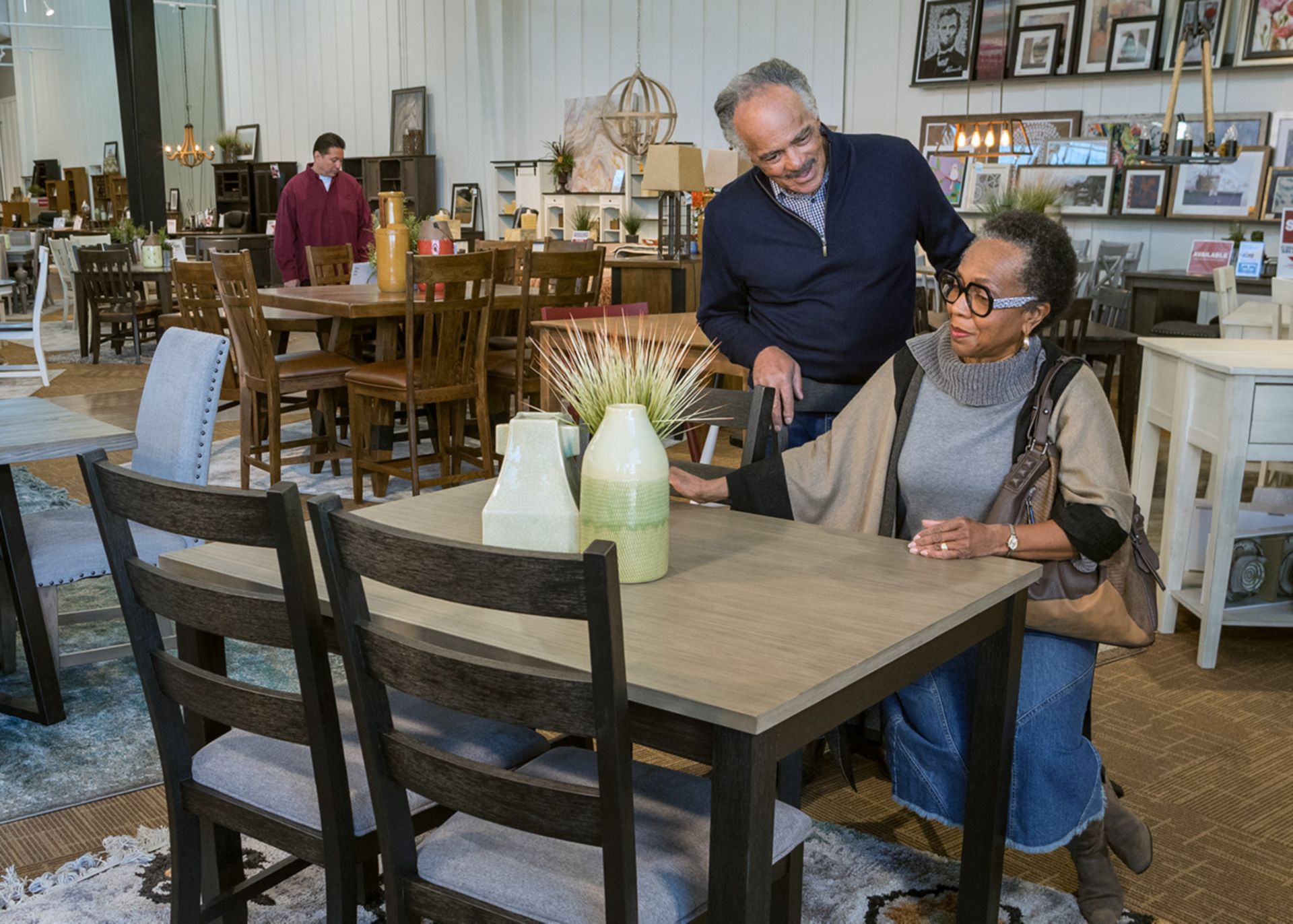 older woman sitting at a dining table in a Furniture Row store while her husband stands behind her