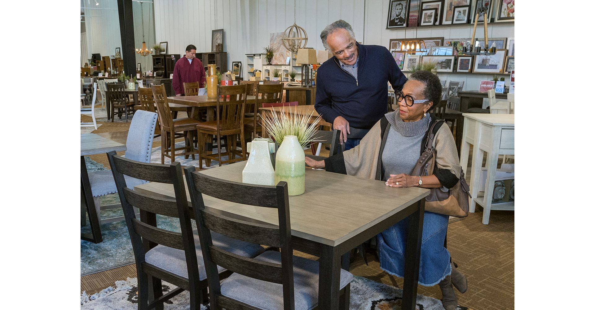 older woman sitting at a dining table in a Furniture Row store while her husband stands behind her